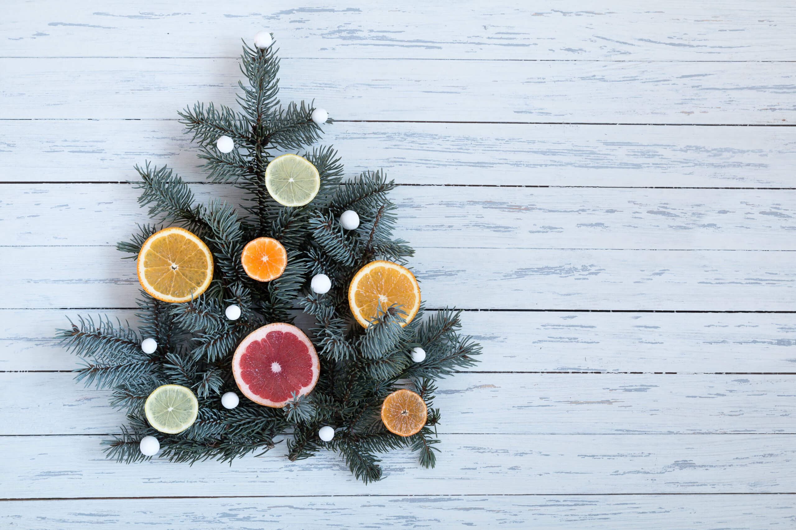Christmas tree with white balls (snowflakes) and oranges tangerines, grapefruits on a white table