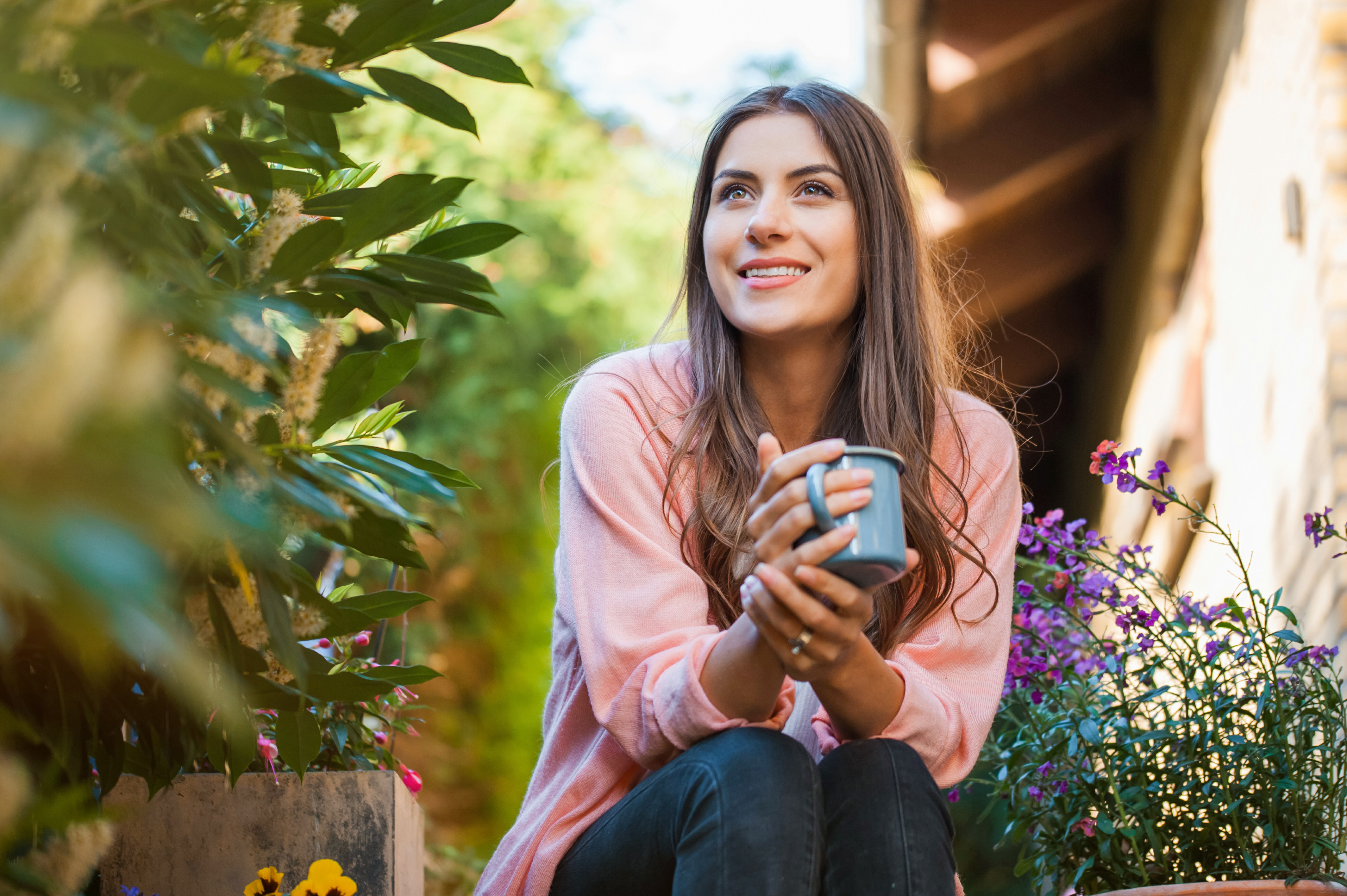 Happy young girl smiling and looking side, sitting on home terrace, holding a mug drinking a hot beverage Hobby and resting leisure concept.