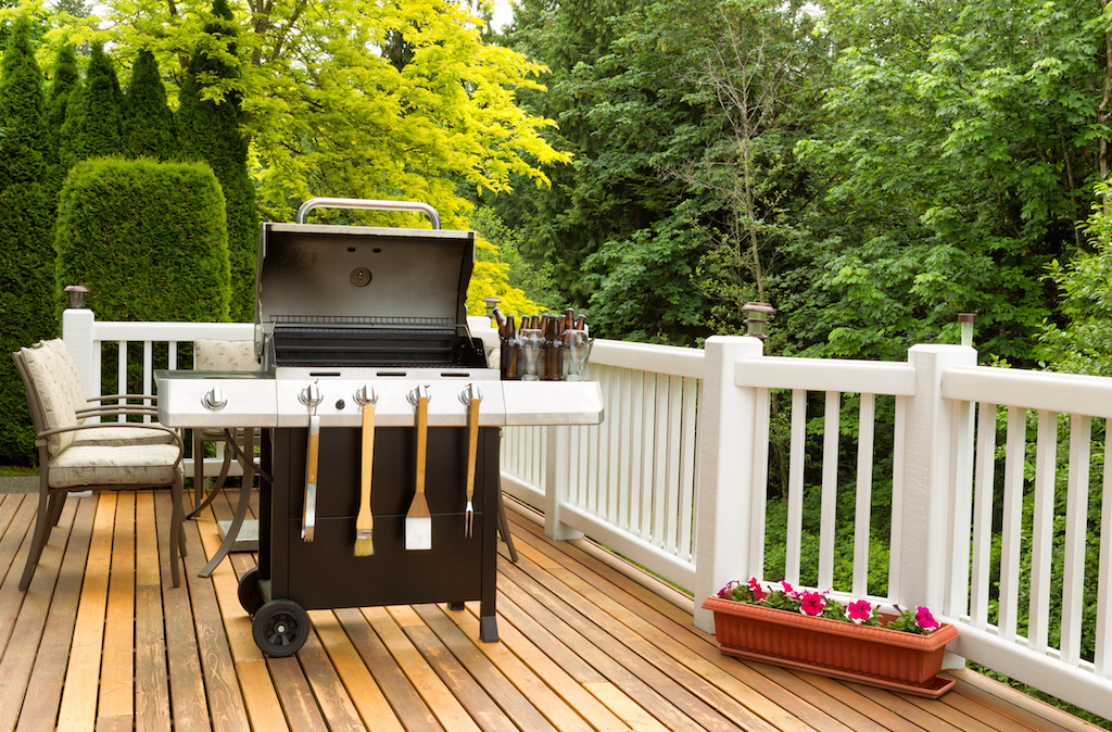 Photo of a clean barbecue cooker with cookware and cold beer in bucket on cedar wood patio. Table and colorful trees in background.